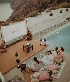 three women sitting on the ground near a swimming pool with candles and lanterns around them