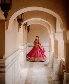 a woman in a red and pink lehenga standing on an archway way with her hands behind her back