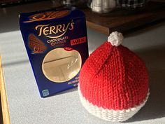 a red and white knitted hat next to a carton of chocolate