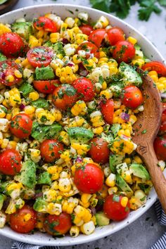 a bowl filled with corn, tomatoes and avocado on top of a table