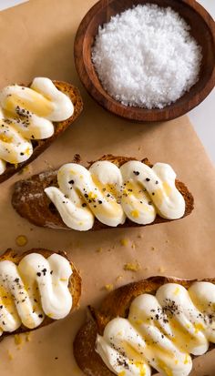 three pieces of bread topped with whipped cream and chocolate sprinkles next to a bowl of sea salt