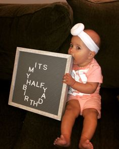 a baby sitting on a couch holding a sign