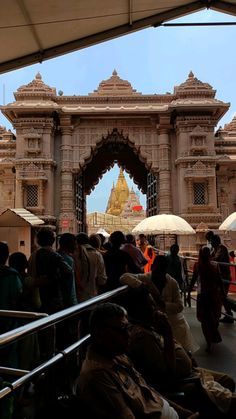 many people are standing in front of an ornate gate with umbrellas over them and one person is sitting on the ground