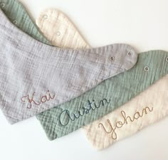 three bibs with embroidered names on them sitting next to each other in different colors