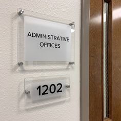 two clear acrylic signs mounted to the side of a wall next to a wooden door