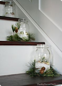 three mason jars filled with pine cones and greenery on top of wooden shelves next to stairs