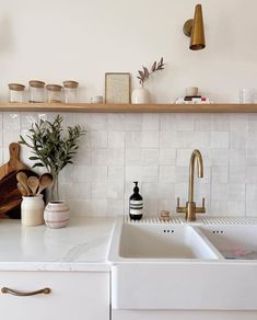 a kitchen with white counter tops and wooden shelves above the sink is decorated with greenery