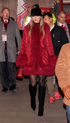 a woman in a red fur coat and hat walking down the street with other people behind her