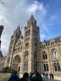 two people are taking pictures in front of a large building with many windows and towers