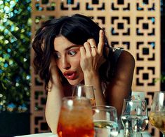 a woman sitting at a table in front of wine glasses with her hand on her head