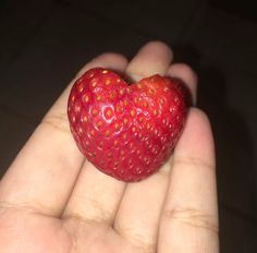 a hand holding a strawberry in the shape of a heart