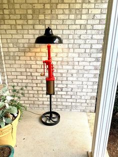 a red lamp sitting on top of a black stand next to a potted plant