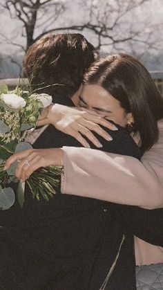 two people hugging each other and holding flowers