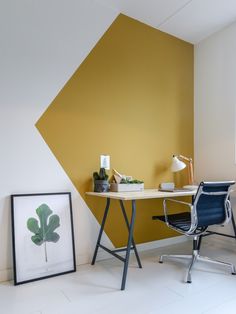 an office with a desk and chair next to a painting on the wall that has a plant in it