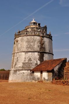 an old round building in the middle of a dirt field with a small house next to it