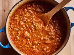 a pot filled with chili and meat on top of a wooden table next to a spoon