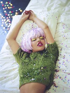 a woman with pink hair laying on a bed covered in confetti and sprinkles