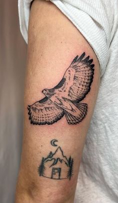 an eagle tattoo on the arm with a house and trees in the background, it is black and white