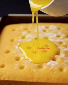 someone pouring yellow sauce on top of a cake