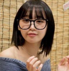 a young woman wearing glasses standing in front of a bamboo wall and looking at the camera