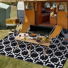 a table and chairs in front of a camper with the door open on grass