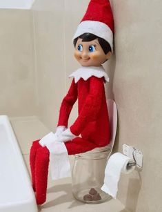 an elf sitting on top of a toilet in a bathroom next to a roll of toilet paper