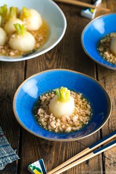 two blue bowls filled with food and chopsticks on top of a wooden table