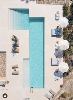 an aerial view of a swimming pool with lounge chairs, umbrellas and tables next to it