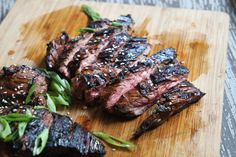 grilled steaks on a wooden cutting board with green garnishes and sesame seeds