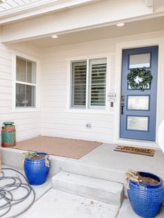 two blue planters sitting on the front steps of a white house with a blue door