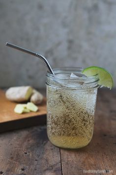 a glass filled with liquid next to a wooden cutting board and lime slice on the table