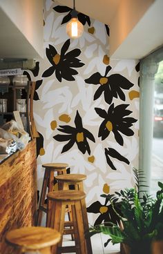 a wall with black and yellow flowers on it next to stools in front of a window