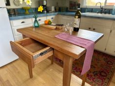 a wooden table with a wine bottle and glasses on it in a kitchen next to a refrigerator