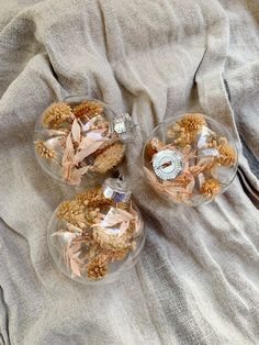 three clear glass dishes with dried flowers in them on a gray cloth covered tablecloth