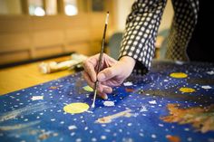 a person holding a paintbrush and painting on a blue surface with yellow circles around it