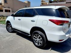 the rear end of a white suv parked in front of a building on a sunny day