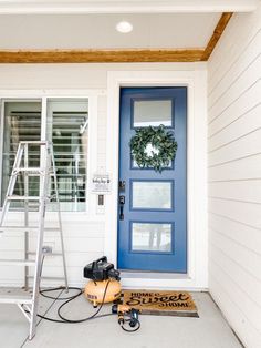 a blue front door with a wreath on it and a ladder next to it in front of a white house