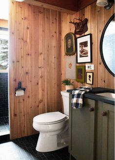 a white toilet sitting in a bathroom next to a wooden paneled wall with pictures on it