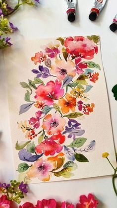 watercolor flowers on paper next to markers and paintbrushes with marker pens in the background