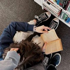 two people sitting on the floor with books in front of them and one person holding an open book