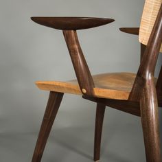 a wooden chair that is sitting up against a gray background with the seat turned down