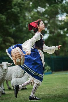 a woman in a blue dress and red hat is dancing with sheep on the grass