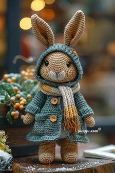 a crocheted rabbit wearing a green coat and scarf, standing on top of a tree stump