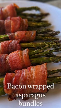 bacon wrapped asparagus bundles on a white plate with the words bacon wrapped asparagus bundles