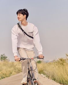 a young man riding a bike down a road next to tall grass and bushes on either side of the road