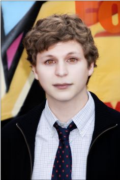 a young man with curly hair wearing a suit and tie in front of a colorful background