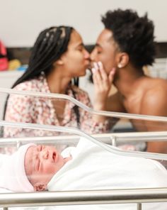 two women are looking at a baby in a hospital bed and one is holding her nose to the other's mouth