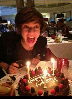 a woman is excited about her birthday cake with lit candles on the table in front of her