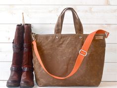 a pair of brown boots sitting next to a brown and orange purse on top of a white wall