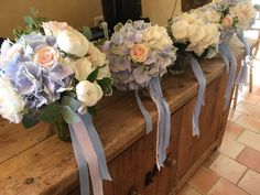 three bouquets of flowers sit on top of a wooden bench with ribbons tied around them